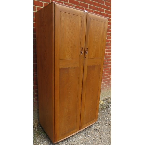 714 - A mid-century blonde elm Windsor double wardrobe by Ercol, the doors opening onto a hanging rail, ra... 