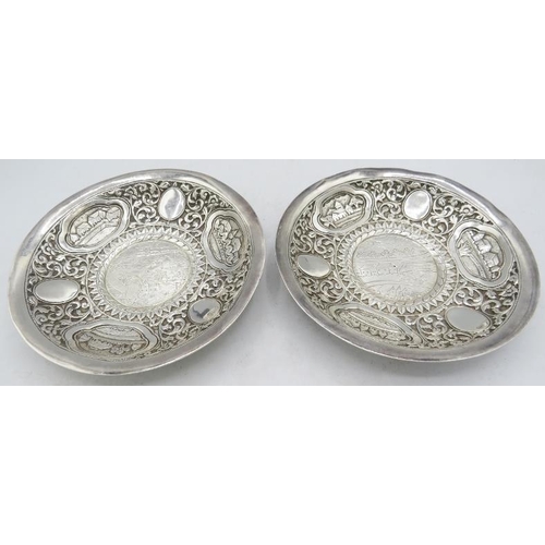 303 - A pair of white Anglo Indian metal dishes heavily embossed with foliate design and cartouche of vill... 