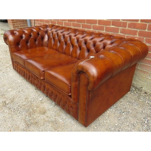 710 - A vintage three-seater Chesterfield sofa upholstered in tobacco brown buttoned leather, raised on ca... 