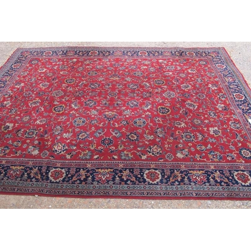 937 - A large mid 20th century Persian carpet, floral pattern on a red ground with deep blue on red border... 