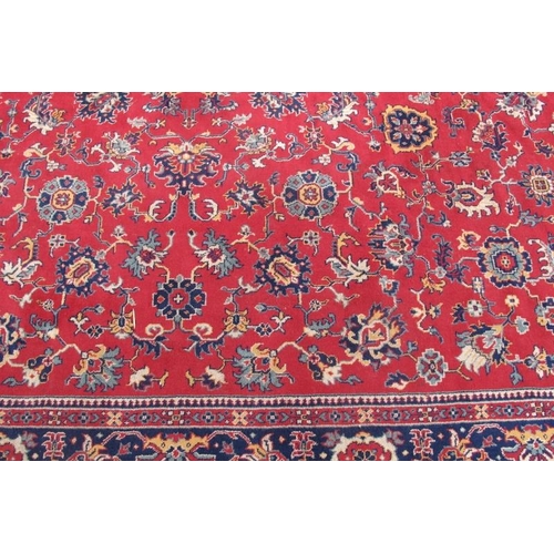 937 - A large mid 20th century Persian carpet, floral pattern on a red ground with deep blue on red border... 