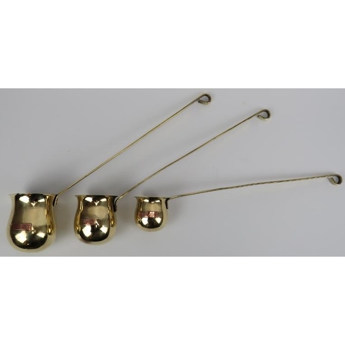 39 - A set of three brassed white metal and copper whisky, rum and brandy ladles, 20th century. Of gradua... 