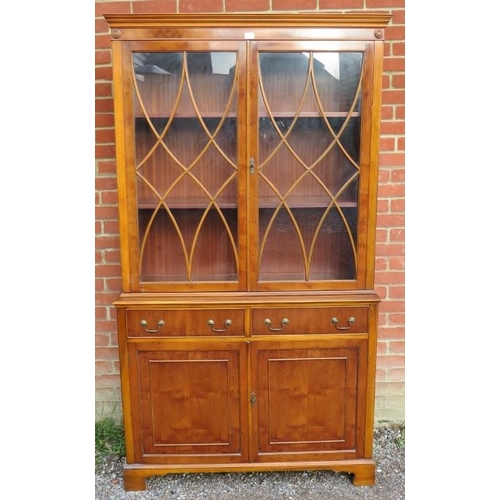 724 - A reproduction yew wood tall glazed bookcase, having tracery doors opening onto two height-adjustabl... 