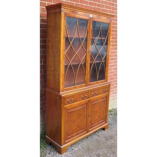 724 - A reproduction yew wood tall glazed bookcase, having tracery doors opening onto two height-adjustabl... 