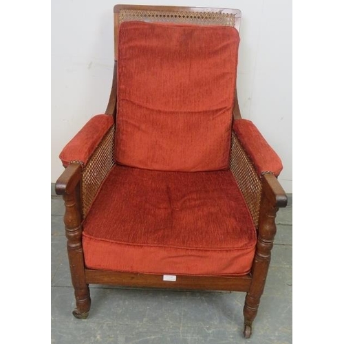 827 - A 19th century mahogany and bergère library chair, with loose cushions upholstered in crimson chenil... 