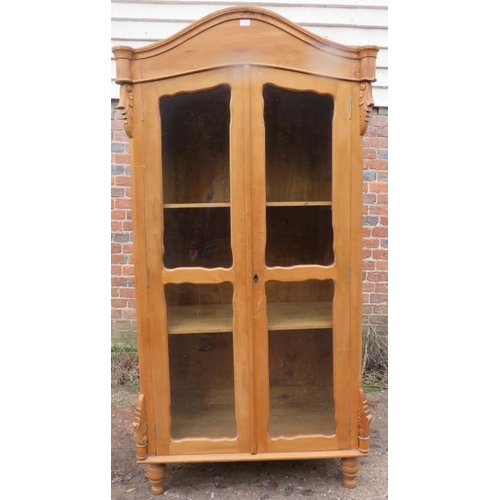 856 - An antique pine Continental glazed display cabinet, the shaped cornice above acanthus carved corbels... 