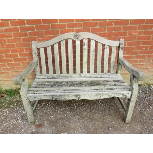 889 - A weathered teak two-seater slatted garden bench, with relief carved rose decoration, on square supp... 