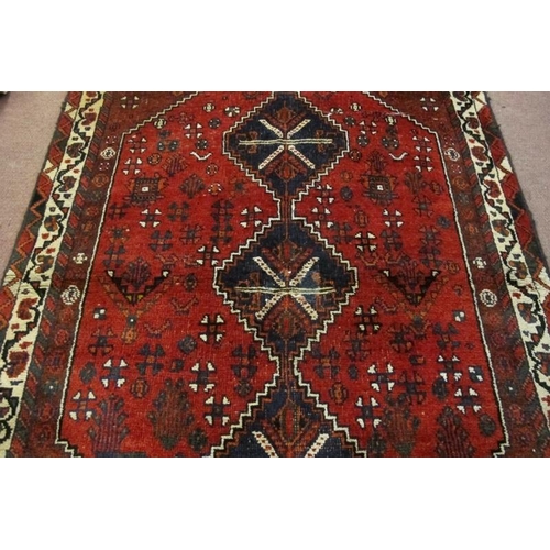 915 - A mid 20th century Persian rug, three central linked medallions on a deep red ground, in good condit... 