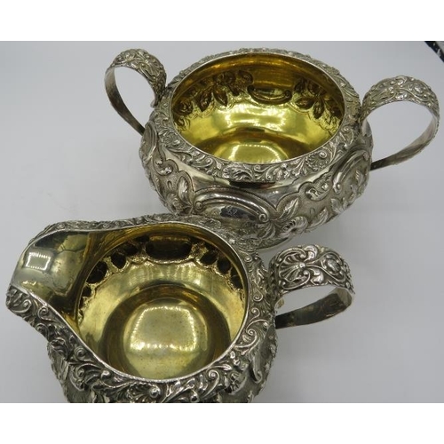 302 - A Georgian heavily embossed silver teapot, sugar bowl & cream jug, sitting on a pedestal base and de... 