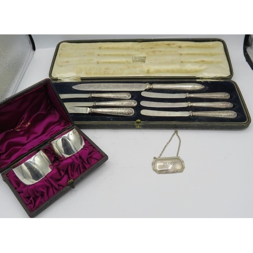 313 - A pair of silver napkin holders, boxed, a silver port label and a boxed set of silver handled tea kn... 