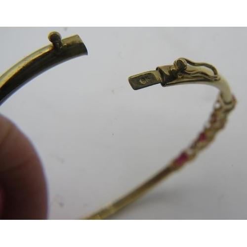 484 - A delicate 9ct yellow gold bangle set with four oval rubies. Each ruby approx 3mm x 5mm, intersperse... 