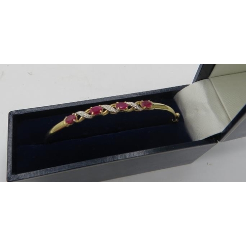 484 - A delicate 9ct yellow gold bangle set with four oval rubies. Each ruby approx 3mm x 5mm, intersperse... 