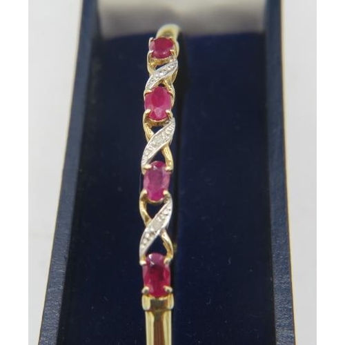 484 - A delicate 9ct yellow gold bangle set with four oval rubies. Each ruby approx 3mm x 5mm, intersperse... 