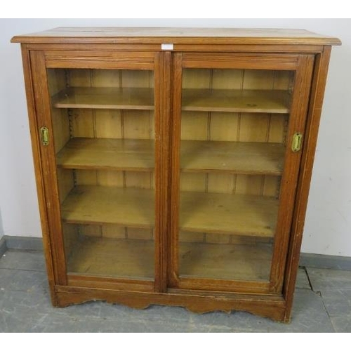 723 - An Edwardian pitch pine glazed cabinet, the two sliding doors with recessed brass handles opening on... 