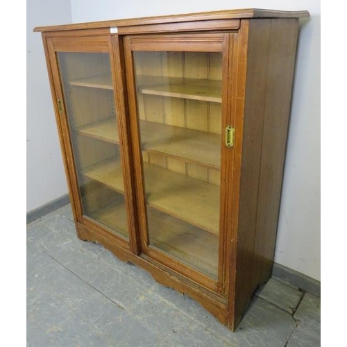 723 - An Edwardian pitch pine glazed cabinet, the two sliding doors with recessed brass handles opening on... 