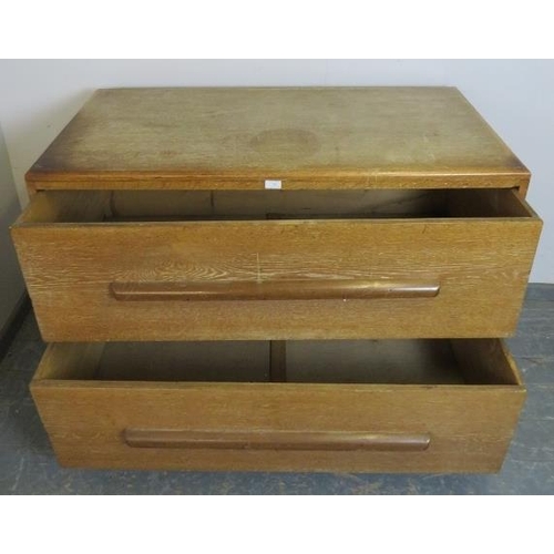 765 - An Art Deco limed oak chest housing two long and deep drawers with scalloped handles, on a plinth ba... 