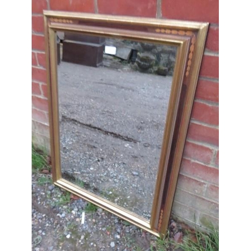 851 - A rectangular bevelled wall mirror within a parcel gilt and inlaid surround. 
H82cm W62cm (approx).
... 