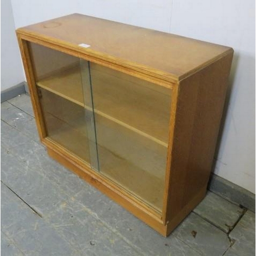 878 - A small vintage mid-century light oak bookcase by G Plan, the sliding glass doors opening onto one h... 