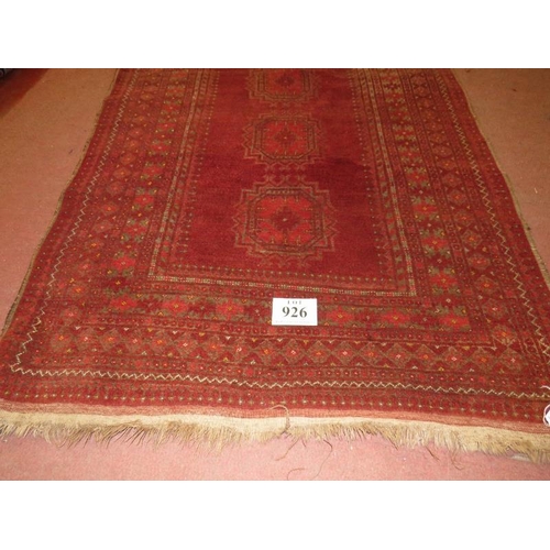 926 - An antique Persian rug, central panel with 3 motifs and deep borders on red ground, 210cm x 128cm.
C... 