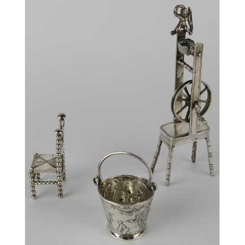 314 - Three miniature continental silver ornaments in the form of a pail, spinning wheel and a chair. The ... 