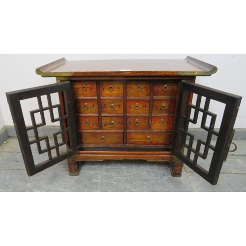 708 - An antique Chinese elm apothecary cabinet with brass mounts, the tracery doors opening onto a select... 