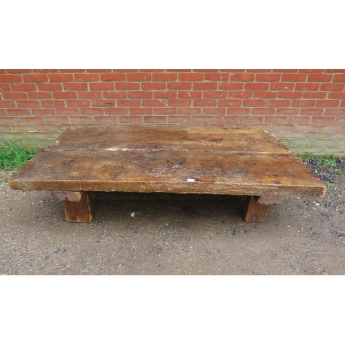 718 - A heavy rustic oak coffee table, constructed of medieval timber, the planked top raised on block fee... 