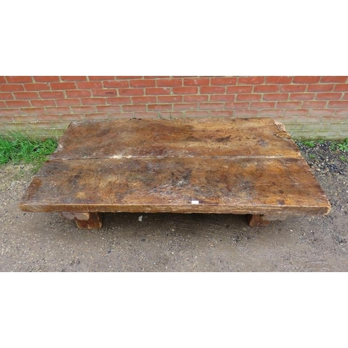 718 - A heavy rustic oak coffee table, constructed of medieval timber, the planked top raised on block fee... 