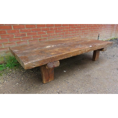 718 - A heavy rustic oak coffee table, constructed of medieval timber, the planked top raised on block fee... 