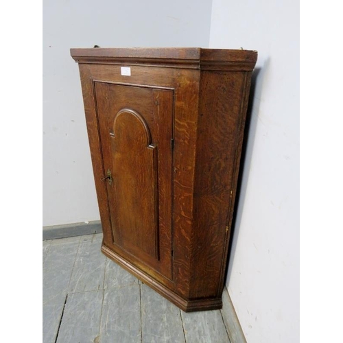 726 - A Georgian oak hanging corner cupboard, the door with arched panel decoration, opening onto two fitt... 