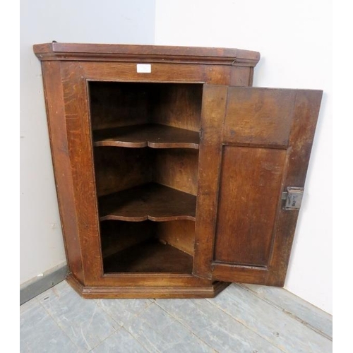 726 - A Georgian oak hanging corner cupboard, the door with arched panel decoration, opening onto two fitt... 