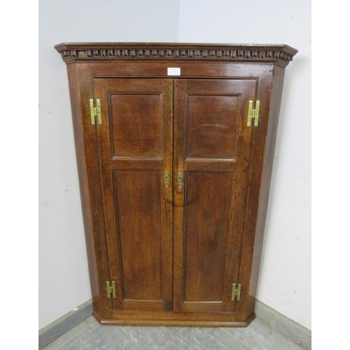 735 - A Georgian oak hanging corner cupboard, the moulded dentil cornice above twin panelled doors with th... 