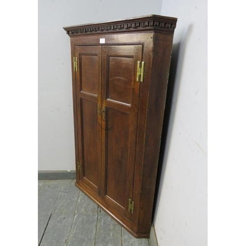 735 - A Georgian oak hanging corner cupboard, the moulded dentil cornice above twin panelled doors with th... 