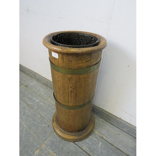 764 - An early 20th century coopered light oak cylinder stick stand, having a tin liner, on a plinth base.... 