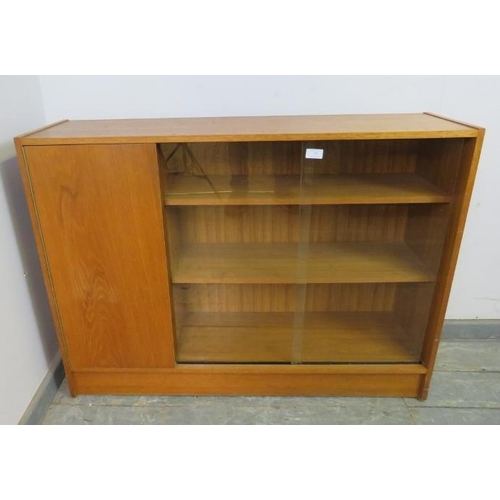 879 - A mid-century teak low enclosed bookcase, having sliding glass doors opening onto two loose shelves,... 