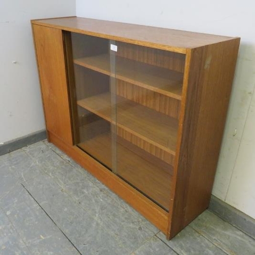 879 - A mid-century teak low enclosed bookcase, having sliding glass doors opening onto two loose shelves,... 