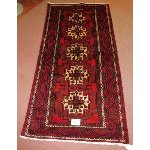 908 - North East Persian Meshed Belouch rug, five central repeat motifs, cream on red ground. 235cm x 116c... 