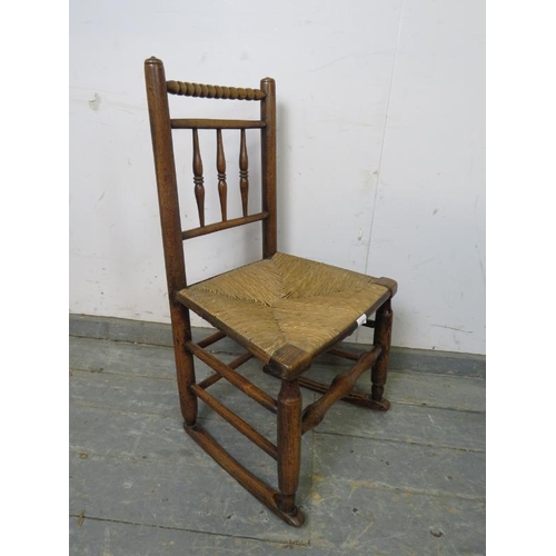 816 - A 19th century child’s elm rocking chair in the Sussex style, the turned back spindles above a rush ... 