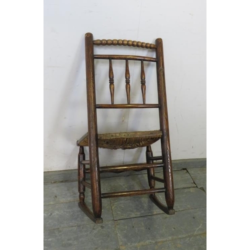 816 - A 19th century child’s elm rocking chair in the Sussex style, the turned back spindles above a rush ... 