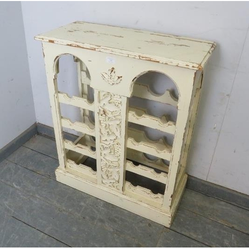 725 - A painted and distressed freestanding wine rack, the relief carved central panel depicting fruiting ... 