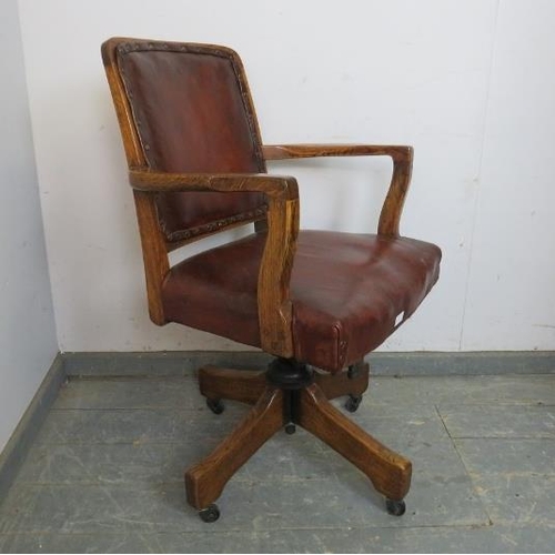 823 - An antique oak swivel and height adjust desk chair, upholstered in burgundy leather with brass studs... 