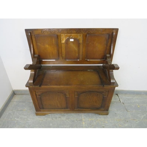 737 - A reproduction oak monk’s bench, the panelled back with lunette carved frieze, above a box settle ba... 