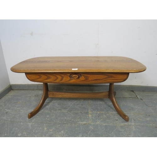 751 - A vintage elm rectangular coffee table in the manner of Ercol, having one lone frieze drawer, on cur... 