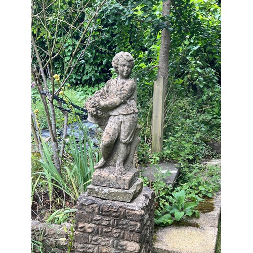 837 - A weathered reconstituted stone garden statue modelled as a young boy carrying a basket of fruit, on... 