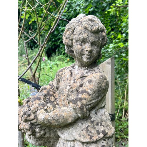 837 - A weathered reconstituted stone garden statue modelled as a young boy carrying a basket of fruit, on... 