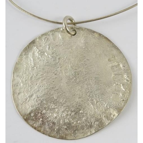 448 - A large silver Artisanal disc pendant, 7.8cm diameter approx, on silver wire collar, with feature ha... 