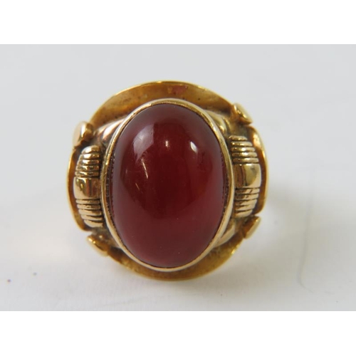 470 - A cabochon Cornelian agate ring, bezel set in an elaborate precious yellow metal setting testing as ... 