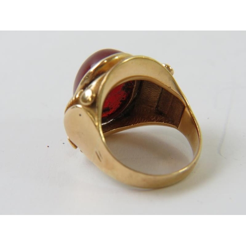 470 - A cabochon Cornelian agate ring, bezel set in an elaborate precious yellow metal setting testing as ... 