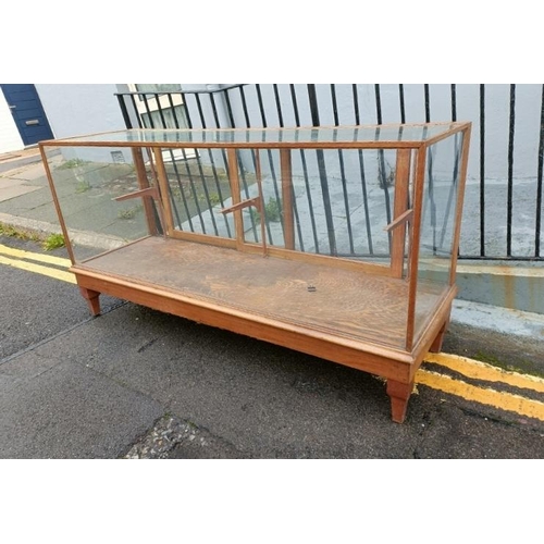 704 - An early 20th century light oak shop display counter, the twin sliding doors opening onto a fully gl... 