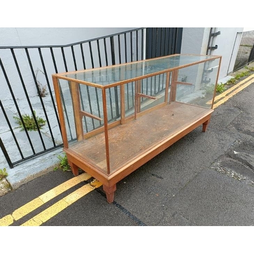 704 - An early 20th century light oak shop display counter, the twin sliding doors opening onto a fully gl... 