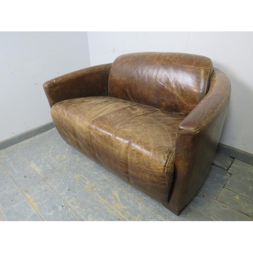 708 - A small two-seater sofa in the aviator style, upholstered in distressed brown leather, on block feet... 